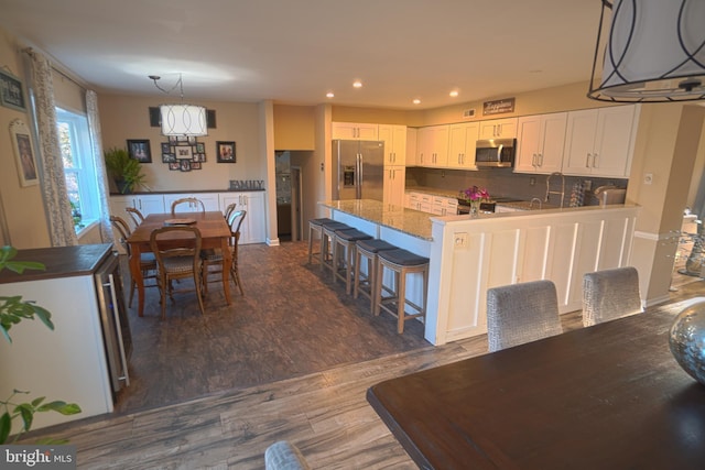 kitchen with a kitchen bar, backsplash, white cabinetry, stainless steel appliances, and dark wood-type flooring