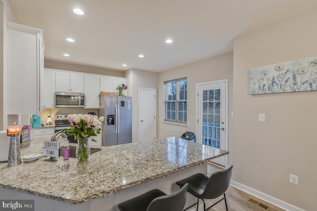 kitchen featuring light stone countertops, kitchen peninsula, white cabinets, and appliances with stainless steel finishes