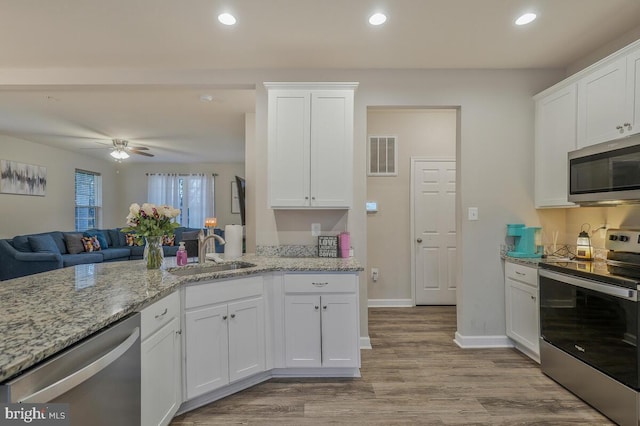 kitchen featuring sink, white cabinetry, appliances with stainless steel finishes, light stone countertops, and light hardwood / wood-style floors