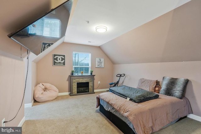 carpeted bedroom with lofted ceiling and a stone fireplace