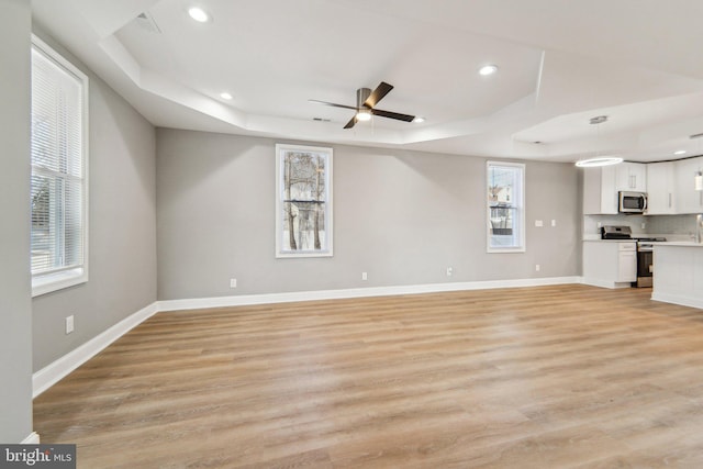 unfurnished living room with a raised ceiling, ceiling fan, and light wood-type flooring