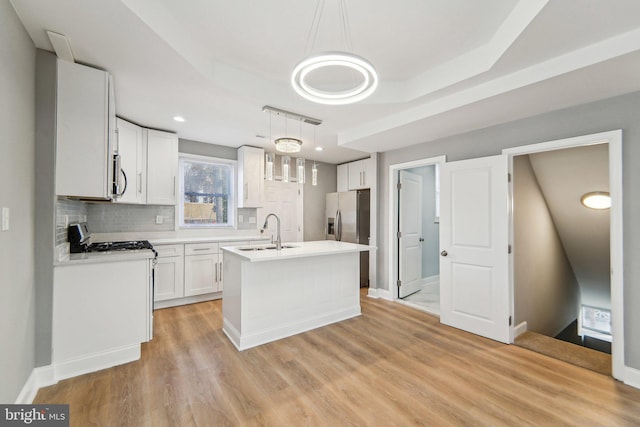 kitchen featuring sink, decorative light fixtures, a center island with sink, stainless steel appliances, and white cabinets