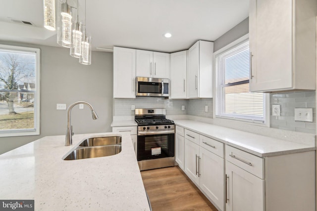 kitchen featuring decorative light fixtures, white cabinetry, sink, light stone counters, and stainless steel appliances