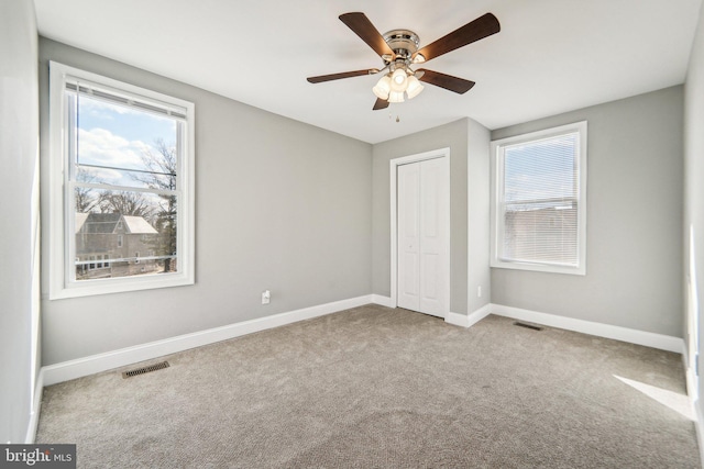 unfurnished bedroom featuring multiple windows, light colored carpet, a closet, and ceiling fan