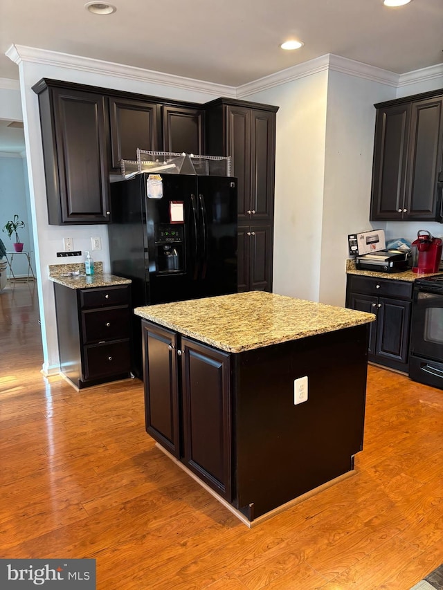 kitchen with a center island, black appliances, crown molding, light stone countertops, and light hardwood / wood-style flooring