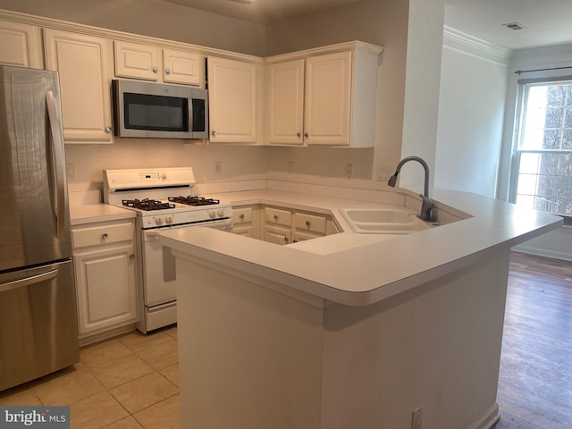 kitchen featuring light tile patterned flooring, sink, white cabinetry, appliances with stainless steel finishes, and kitchen peninsula