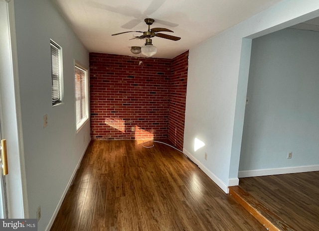 empty room with ceiling fan, brick wall, and dark hardwood / wood-style floors