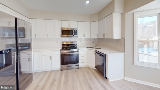 kitchen featuring appliances with stainless steel finishes, sink, white cabinets, light stone counters, and light wood-type flooring