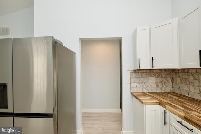 kitchen featuring tasteful backsplash, white cabinetry, stainless steel refrigerator, and wood counters