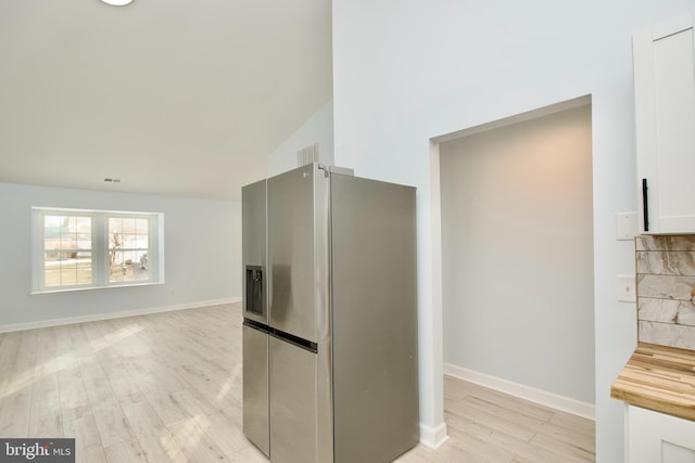 kitchen featuring vaulted ceiling, white cabinetry, decorative backsplash, stainless steel fridge with ice dispenser, and light hardwood / wood-style flooring