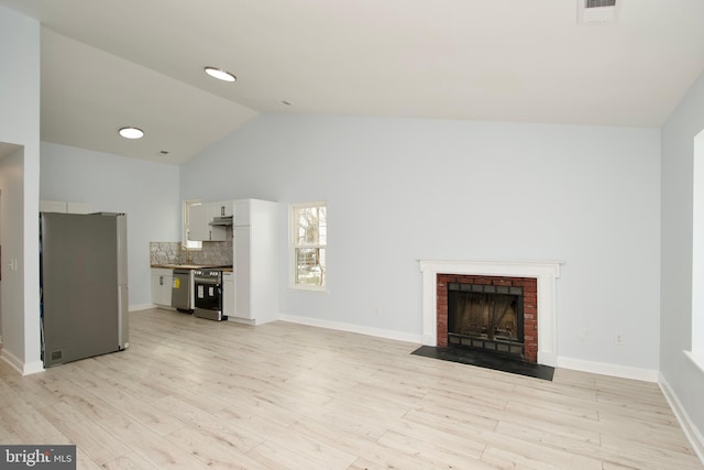 unfurnished living room featuring vaulted ceiling, sink, a fireplace, and light hardwood / wood-style floors