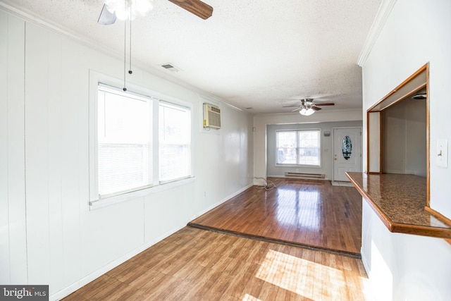 interior space featuring crown molding, hardwood / wood-style flooring, a baseboard heating unit, a wall mounted AC, and a textured ceiling