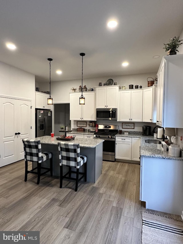 kitchen featuring pendant lighting, appliances with stainless steel finishes, white cabinetry, light stone counters, and a kitchen island