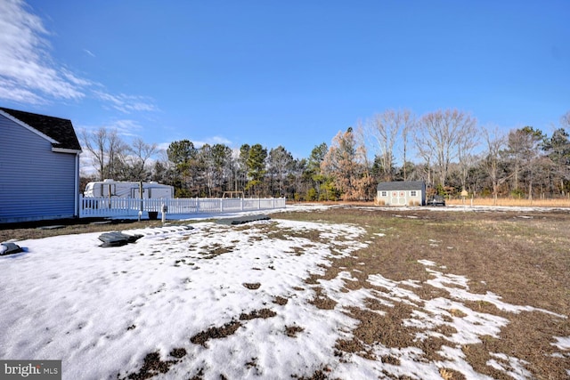 yard covered in snow with a storage shed and a wooden deck