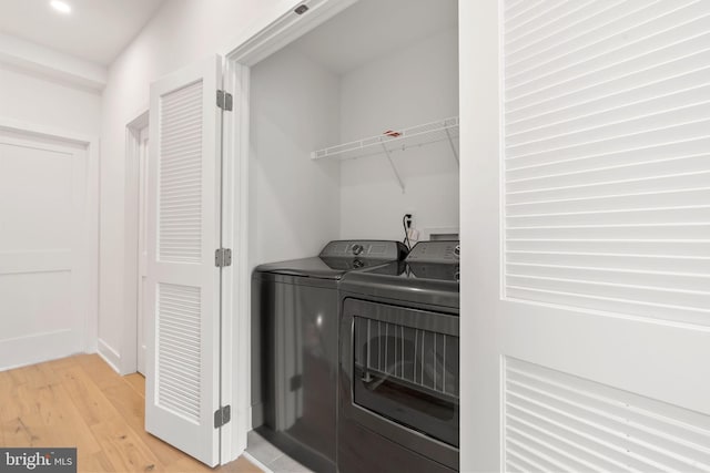 laundry room with washing machine and clothes dryer and light wood-type flooring