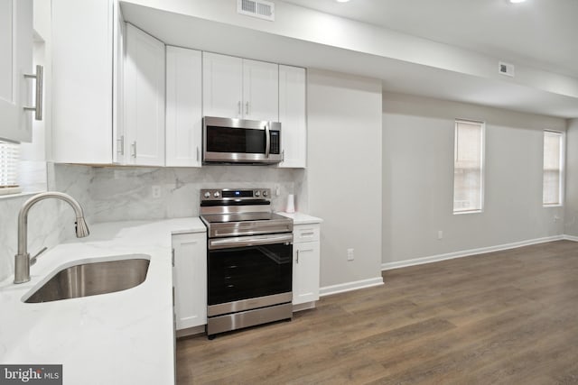 kitchen with sink, white cabinetry, stainless steel appliances, light stone countertops, and decorative backsplash