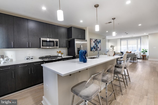 kitchen featuring pendant lighting, a kitchen breakfast bar, an island with sink, and appliances with stainless steel finishes