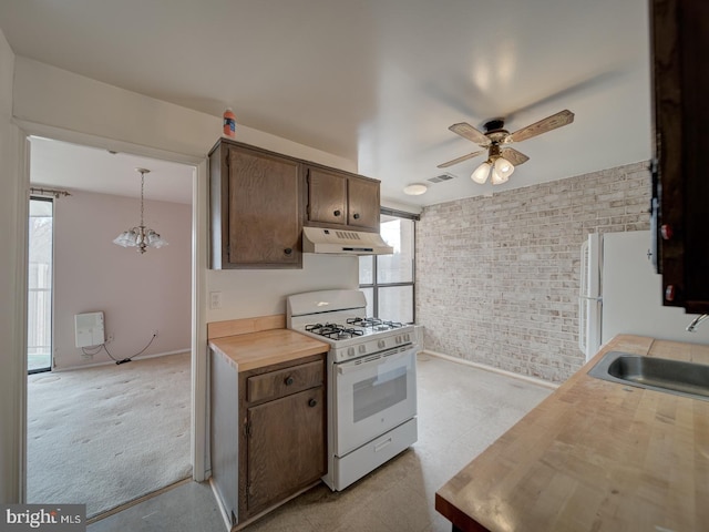 kitchen with pendant lighting, sink, white appliances, ceiling fan, and brick wall