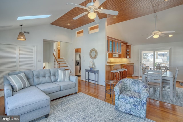 living room with ceiling fan, a skylight, high vaulted ceiling, and light hardwood / wood-style flooring