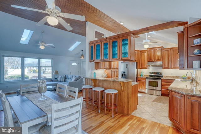 kitchen with light stone countertops, appliances with stainless steel finishes, sink, and vaulted ceiling with skylight