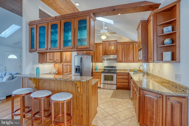 kitchen featuring a breakfast bar area, ceiling fan, appliances with stainless steel finishes, lofted ceiling with skylight, and light stone counters