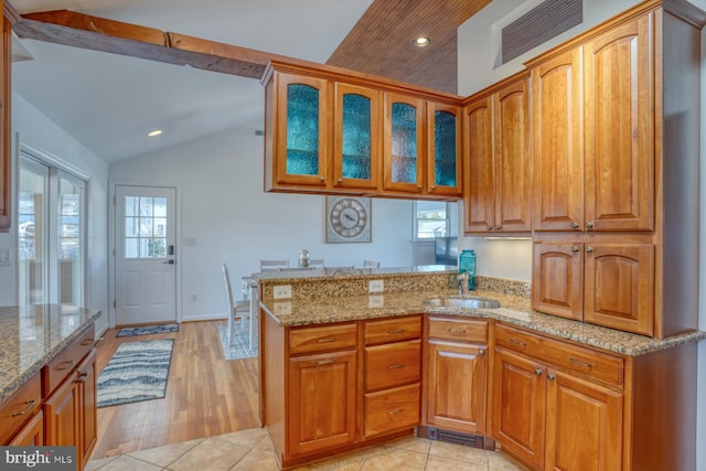 kitchen with vaulted ceiling, sink, light stone counters, and kitchen peninsula