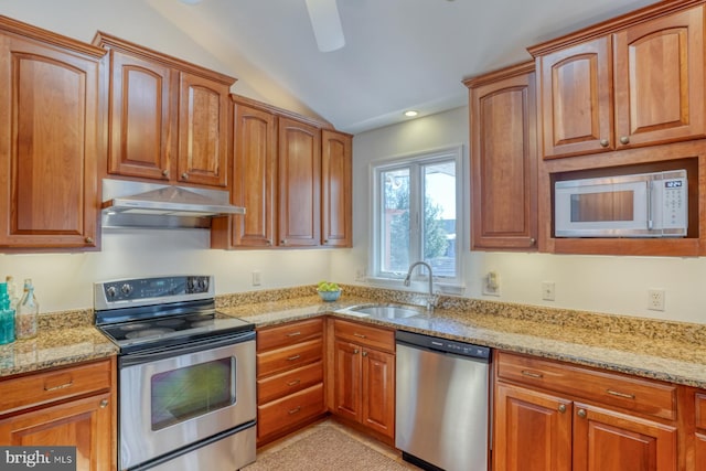 kitchen featuring light stone counters, lofted ceiling, appliances with stainless steel finishes, and sink