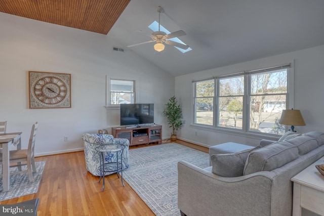 living room with lofted ceiling with skylight, ceiling fan, and light wood-type flooring