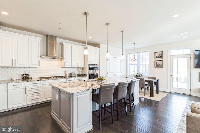 kitchen featuring white cabinetry, wall chimney range hood, and an island with sink