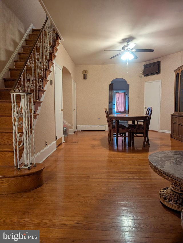 dining space featuring a wall mounted air conditioner, wood-type flooring, ceiling fan, and baseboard heating