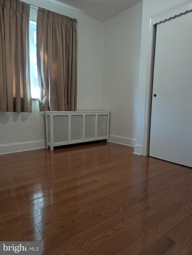 unfurnished room with dark hardwood / wood-style floors and radiator heating unit