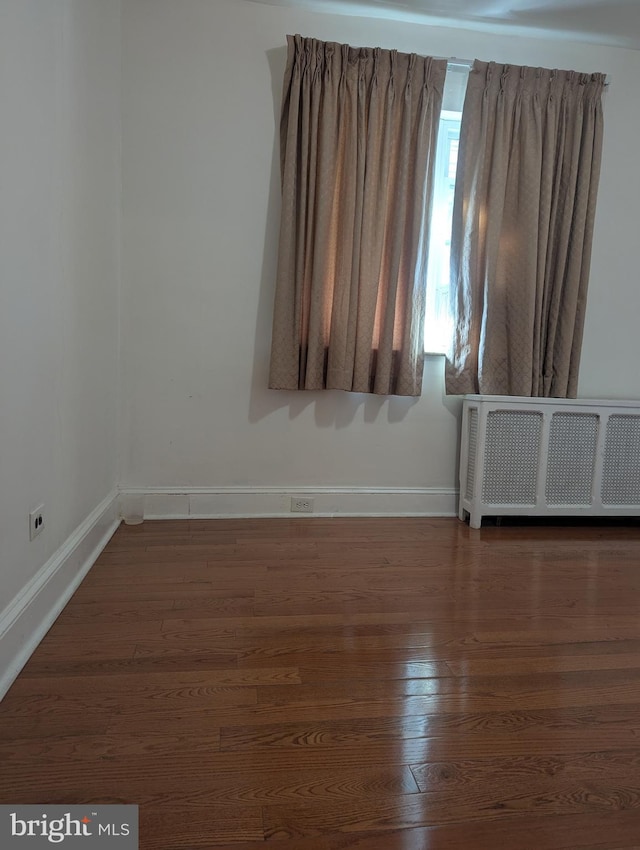 spare room featuring dark wood-type flooring and radiator