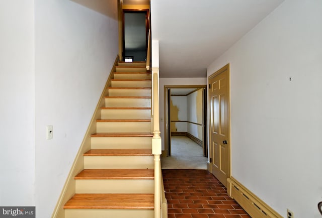 stairway featuring baseboards, brick floor, and a baseboard radiator