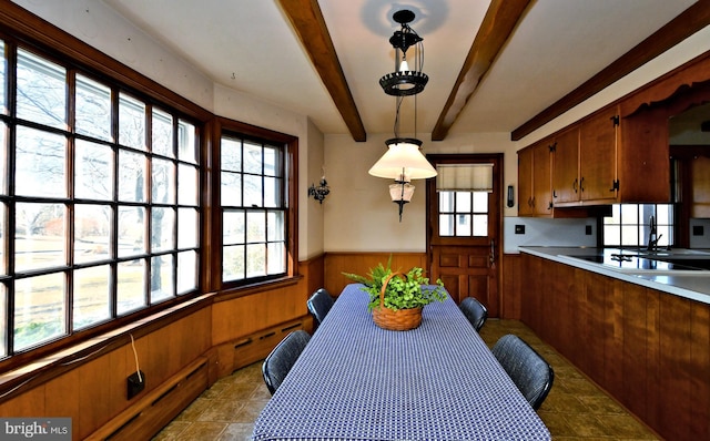 dining area featuring beamed ceiling, wainscoting, and wooden walls