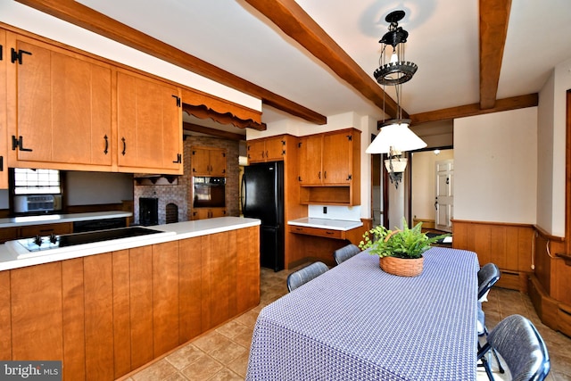 kitchen featuring black appliances, beamed ceiling, brown cabinetry, and a wainscoted wall