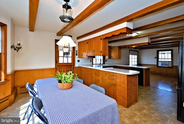 kitchen featuring a wainscoted wall, wood walls, beam ceiling, a peninsula, and brown cabinetry