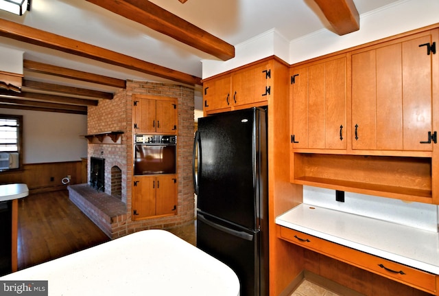 kitchen with beam ceiling, black appliances, brown cabinetry, a fireplace, and wainscoting