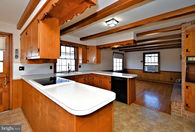 kitchen with beam ceiling, a peninsula, light countertops, black appliances, and wainscoting