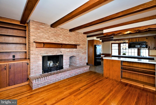 kitchen with beamed ceiling, black appliances, wood finished floors, a fireplace, and light countertops