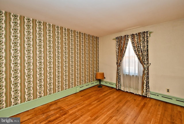 unfurnished room featuring baseboard heating and wood finished floors