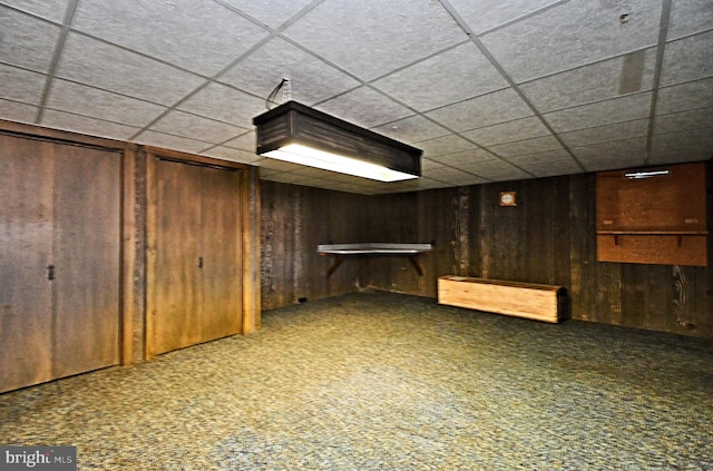 finished basement featuring a drop ceiling, wood walls, and carpet floors