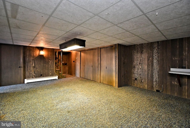 finished basement with stairs, wooden walls, carpet flooring, and a baseboard radiator