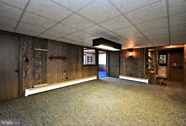 finished basement with stairway, wooden walls, carpet flooring, and a baseboard radiator