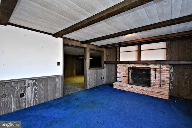 unfurnished living room with beamed ceiling, wood walls, a brick fireplace, and carpet flooring