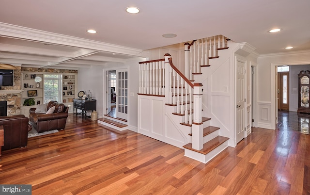 stairs featuring hardwood / wood-style floors, crown molding, a fireplace, and beamed ceiling