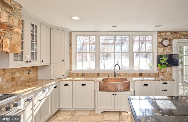 kitchen with sink, light stone countertops, stainless steel range oven, and white cabinets