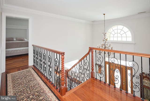 stairway with an inviting chandelier, ornamental molding, and hardwood / wood-style floors