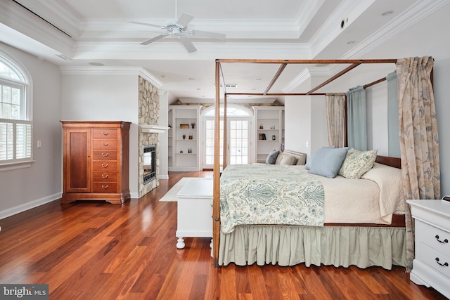 bedroom featuring crown molding, a stone fireplace, dark hardwood / wood-style flooring, and a tray ceiling