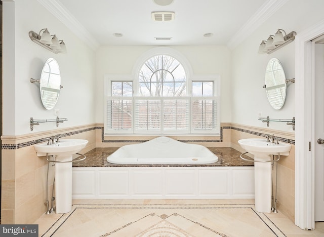 bathroom with dual sinks, crown molding, and tile walls