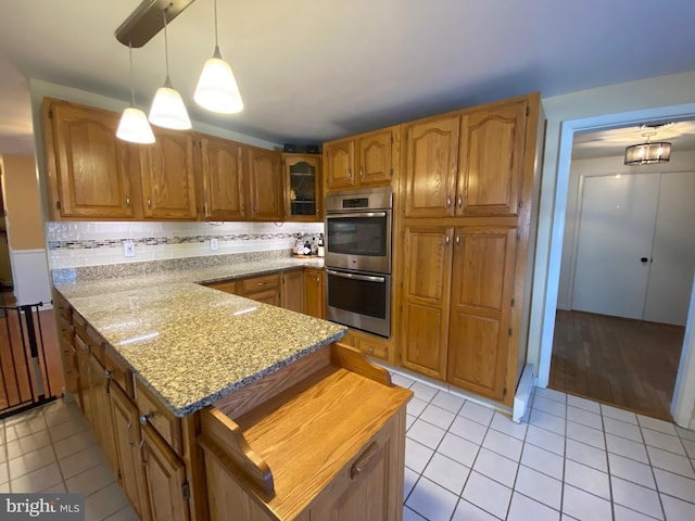 kitchen featuring double oven, backsplash, hanging light fixtures, light stone counters, and light tile patterned flooring